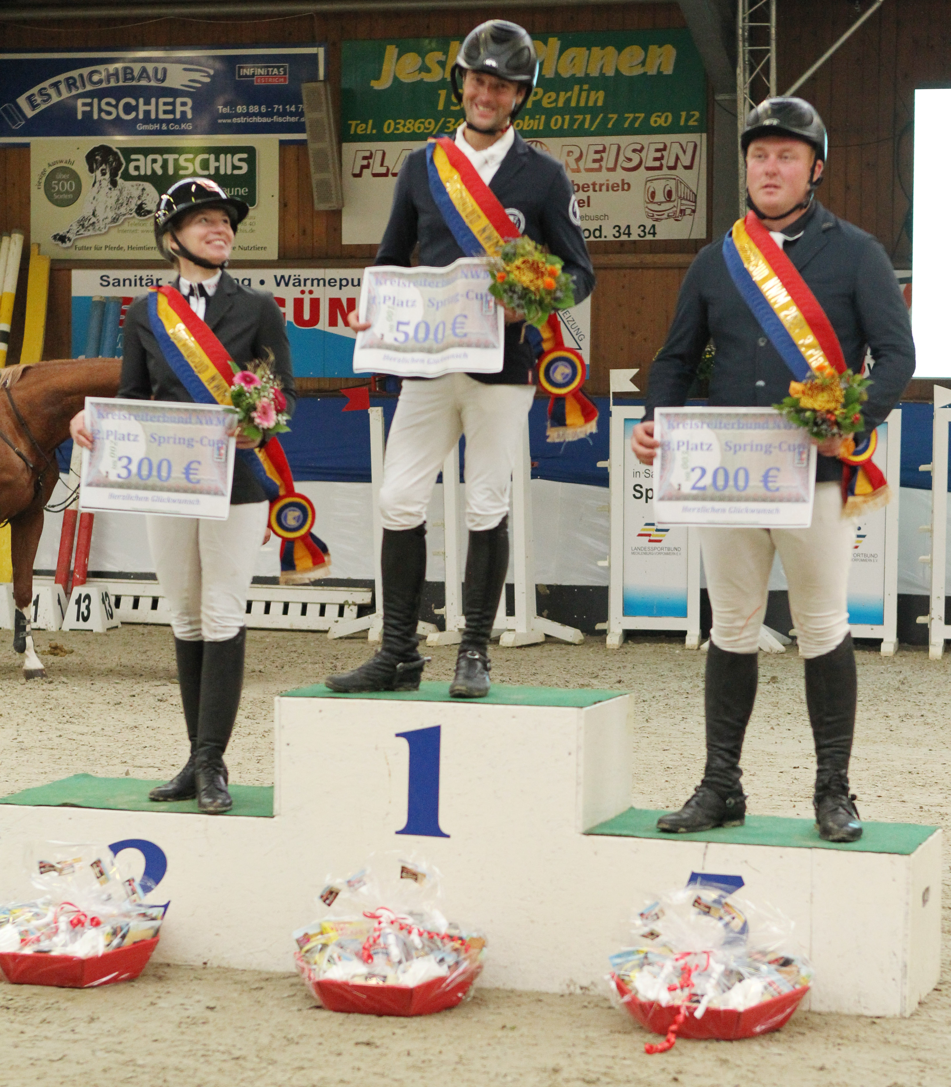 Die drei Erstplatzierten im NWM-Springcup 2021 mit Schärpen des KRB-Nordwestmecklenburg, ihren symbolischen Checks und den gewonnenen Präsenten: Sieger Philipp Makowei, Zweite Juliane Weihs, Dritter Christoph Maack. © Jutta Wego