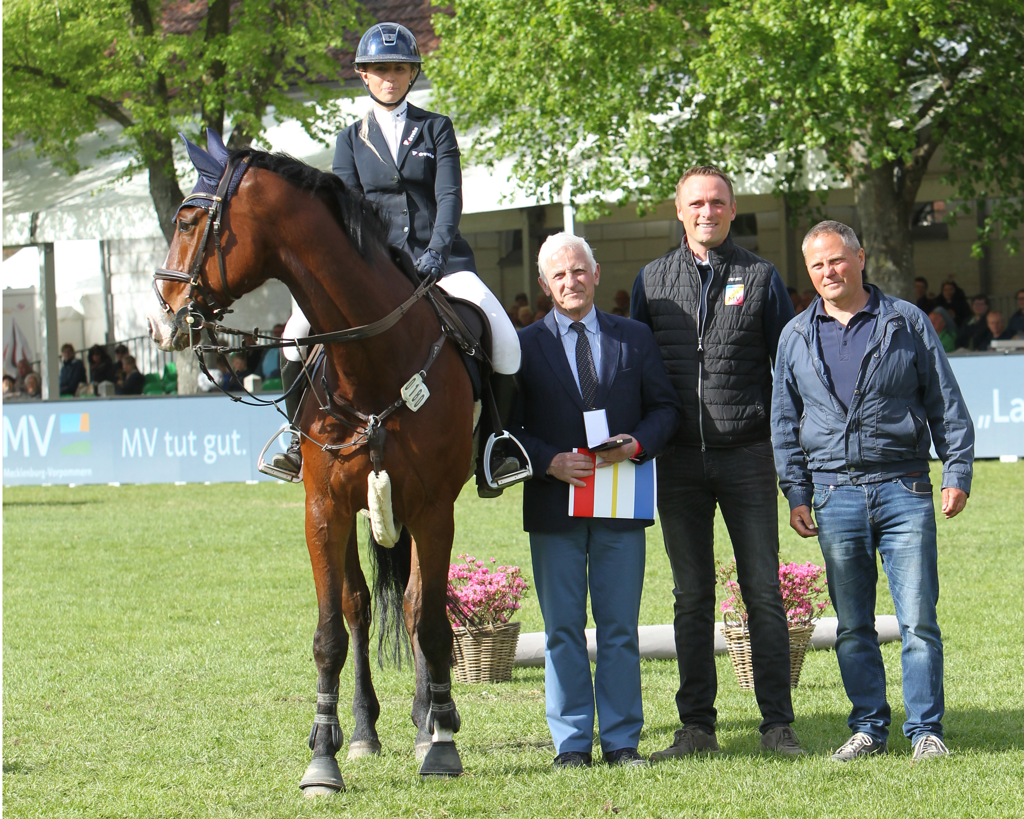 Auf ihrem aktuellen Spitzenpferd Quincy sitzend, überreichte Verbandspräsident Dr. Burkhard Dittmann zusammen mit Landes-Honorartrainer Heiko Strohbehn und Vater Torsten (v.l.) der 23-jährigen Christin Wascher vor großer Kulisse im Landgestüt das „Goldene Reitabzeichen“. © Jutta Wego