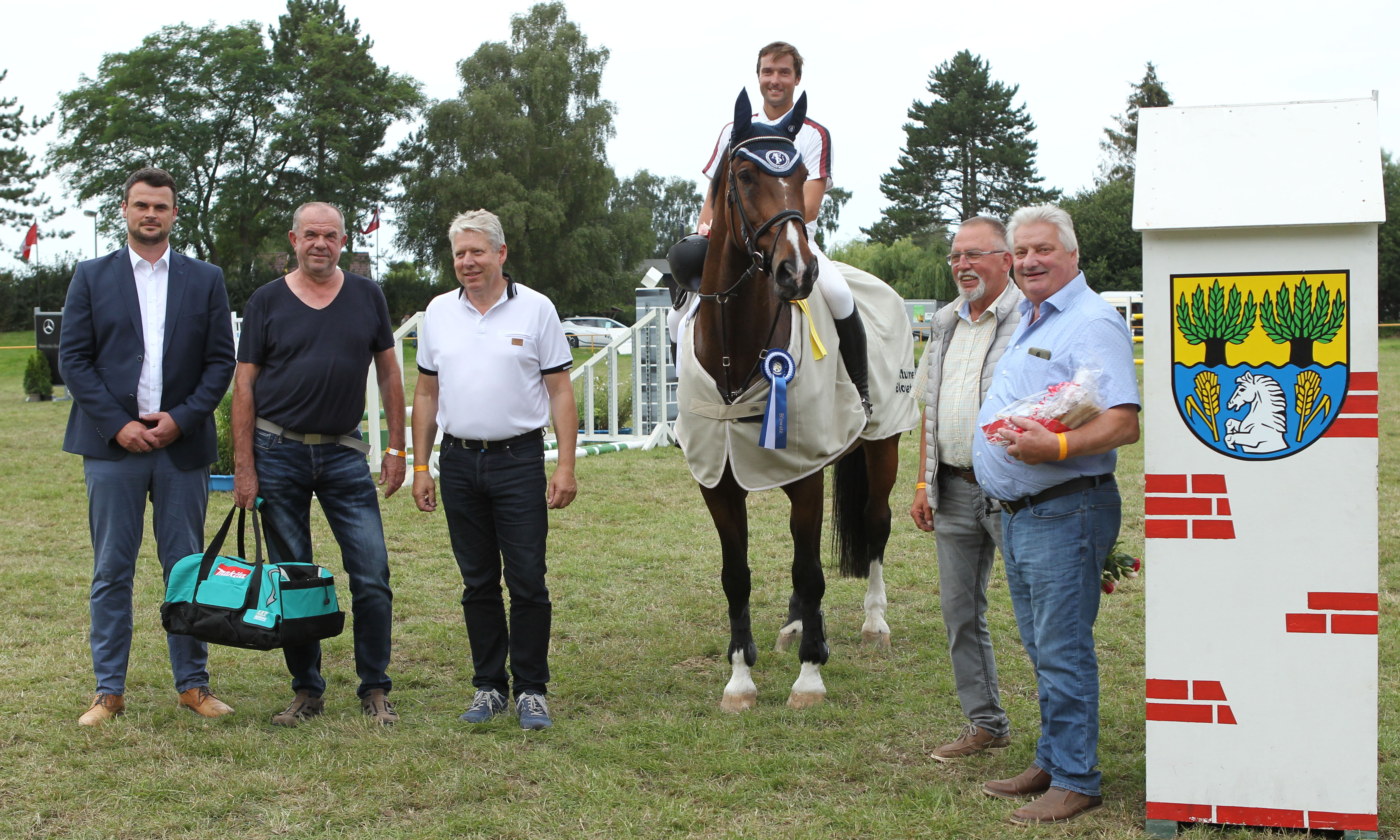 Vor dem Gemeindelogo von Blowatz gratulierten Philipp Makowei zum Sieg: v.l. Landrat Tino Schomann, Winfried Kauert (Stellvertr. Bürgermeister der Gemeinde Blowatz), Kreistagspräsident und Schirmherr Thomas Grothe, Joachim Lenschow von der Turnierleitung und Dr. Lothar Makowei, der Vater des Siegers. © Jutta Wego