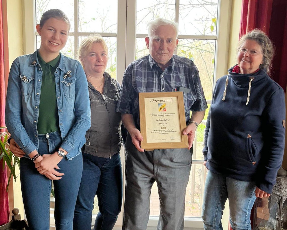 Wolfgang Rehmer erhält im Alter von 86 Jahren aus den Händen von Martina Hermann (r.) im Beisein seiner Tochter Birca Roos (2.v.li.) und Enkelin Stella Baranowski (l.) die Ehrennadel des Landesverbandes Mecklenburg-Vorpommern für Reiten, Fahren und Voltigieren e.V. in Gold. © Familie Roos